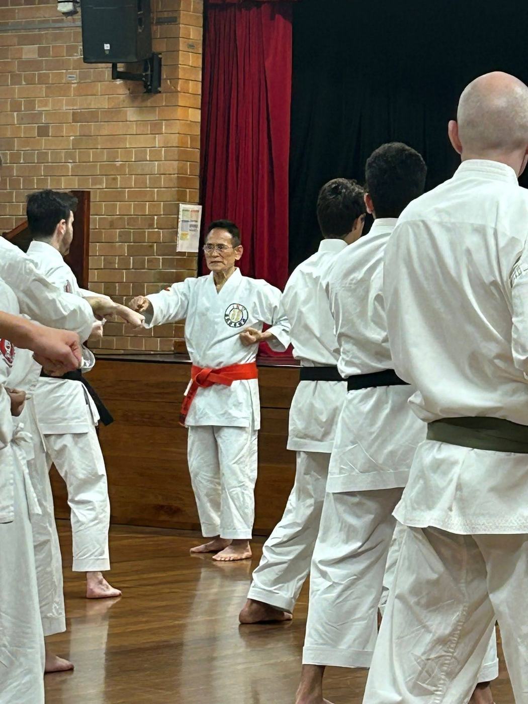 Yamamoto Soshihan, in a red belt, leading a line of black belts through a drill at his 2024 seminar in the Strathfield North hall